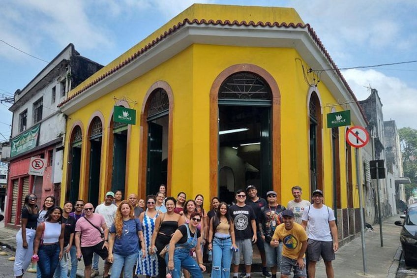 Un grupo de personas frente a un edificio amarillo con ventanas de arco y un letrero verde. 3