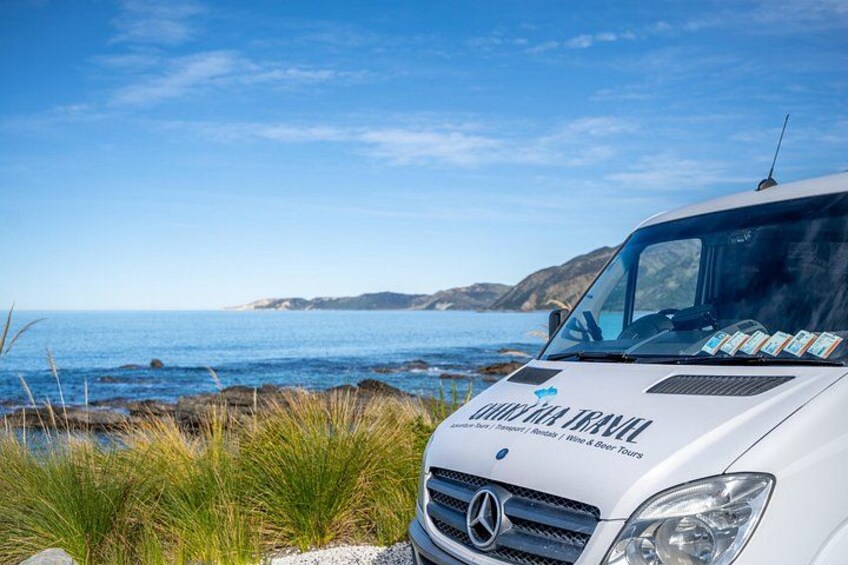 Un camping-car Mercedes-Benz blanc est garé au bord d’une route côtière, avec un ciel bleu dégagé et une mer calme en arrière-plan. 1