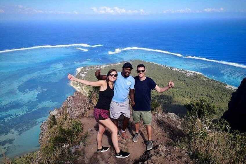 Three people standing on a cliff overlooking a coastline with clear blue waters and a view of the ocean. 1