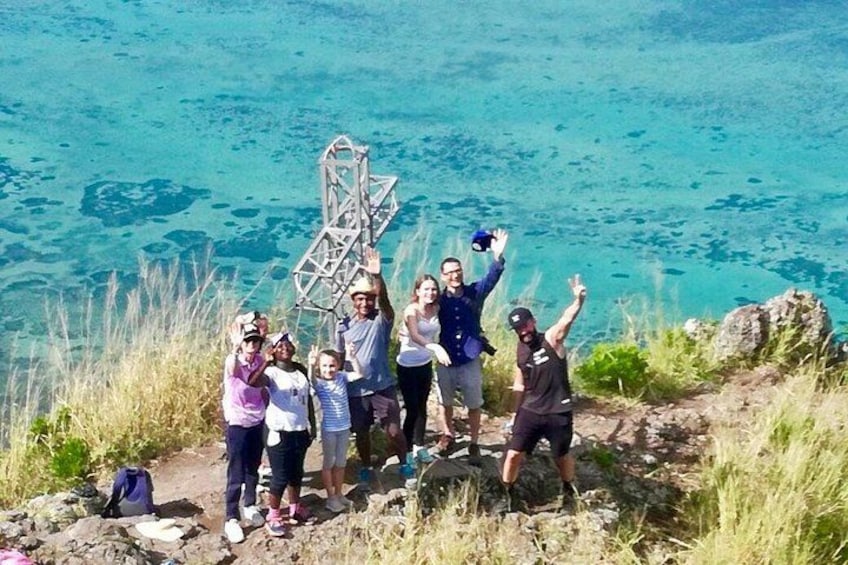 A group of people standing on a rocky outcrop with a metal structure in the background, overlooking a body of water. 4