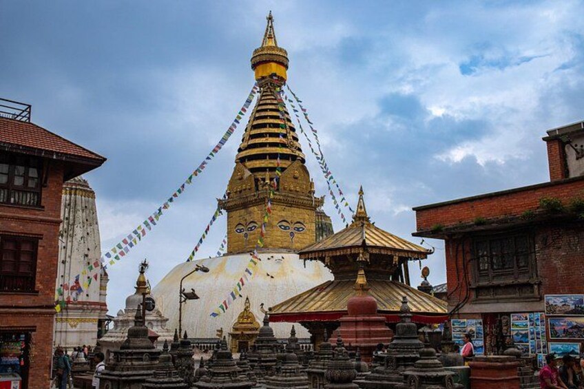 Un gran stupa con una aguja dorada, rodeado de stupas más pequeños y ruecas de oración, con edificios tradicionales de fondo. 3