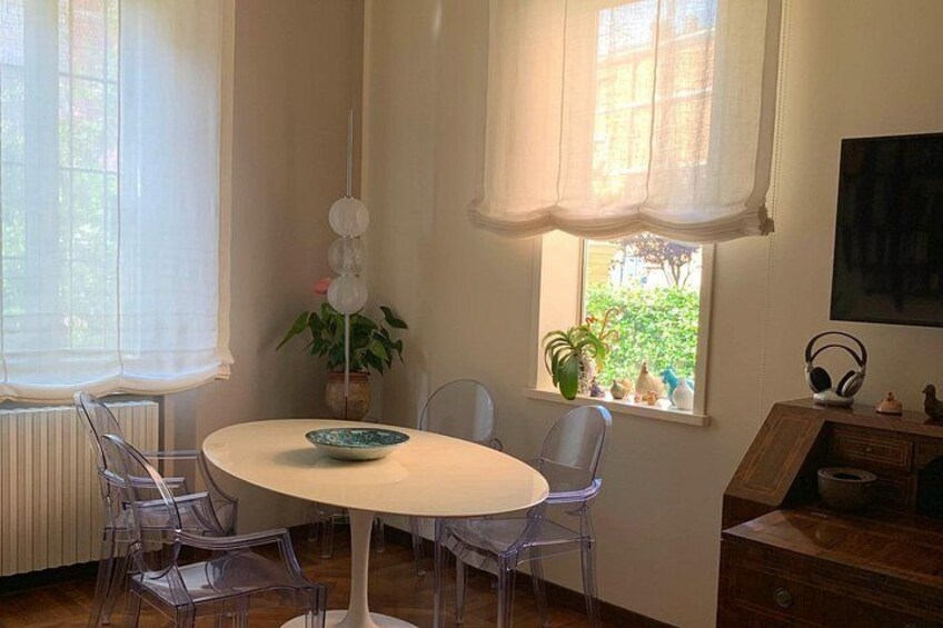 En matplats med ett runt bord, stolar, en skål, en krukväxt och ett fönster med gardiner. 4