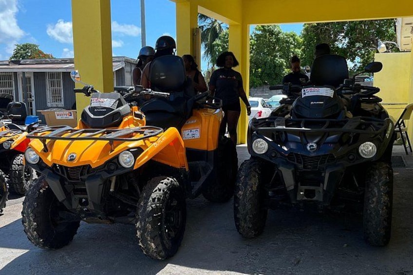 Two ATVs parked under a yellow shelter, with people standing nearby. 3