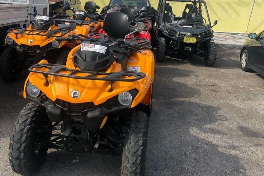 A row of orange ATVs parked in a lot. 4