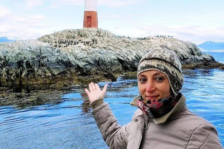 A person standing by a rocky shoreline with a lighthouse in the background. 1