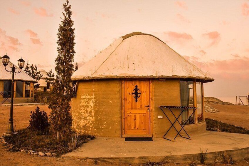 A traditional yurt with a thatched roof, a wooden door, and a small porch area. 2