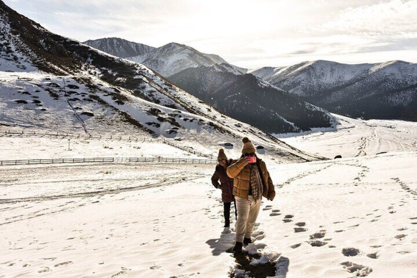 A snowy mountain path with footprints and a fence. 1