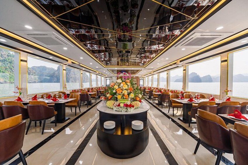 A luxurious dining area with a central floral arrangement, high ceilings, and large windows overlooking a body of water. 3