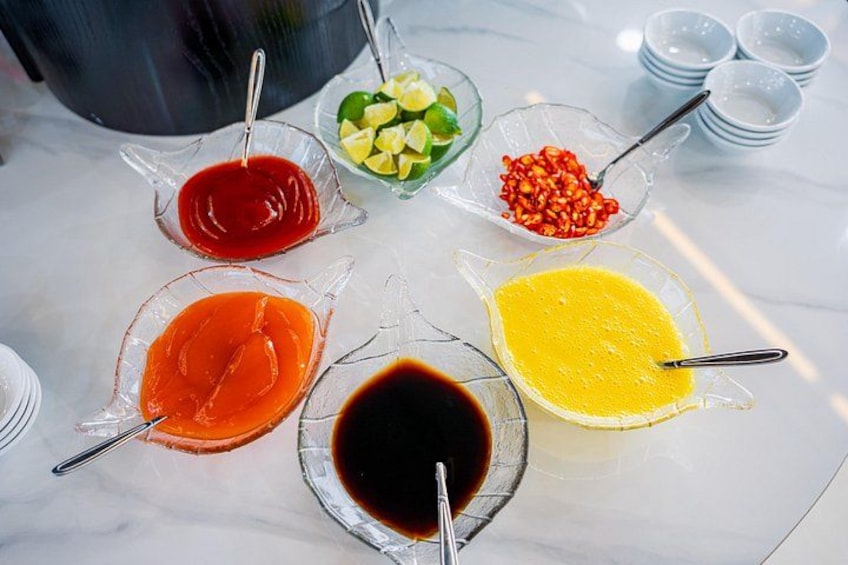 A table with various condiments in glass bowls, including sauces and a yellow liquid. 5