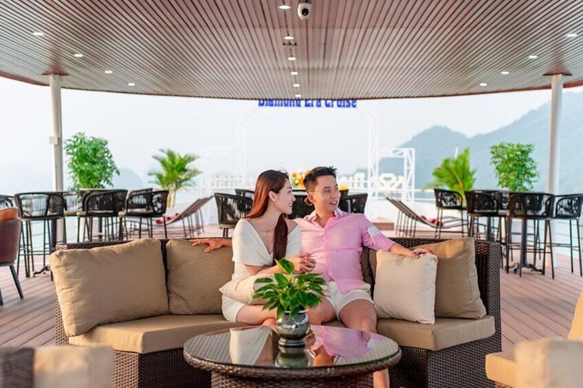 A couple sitting on a cushioned outdoor sofa with a view of the sea and mountains in the background. 3