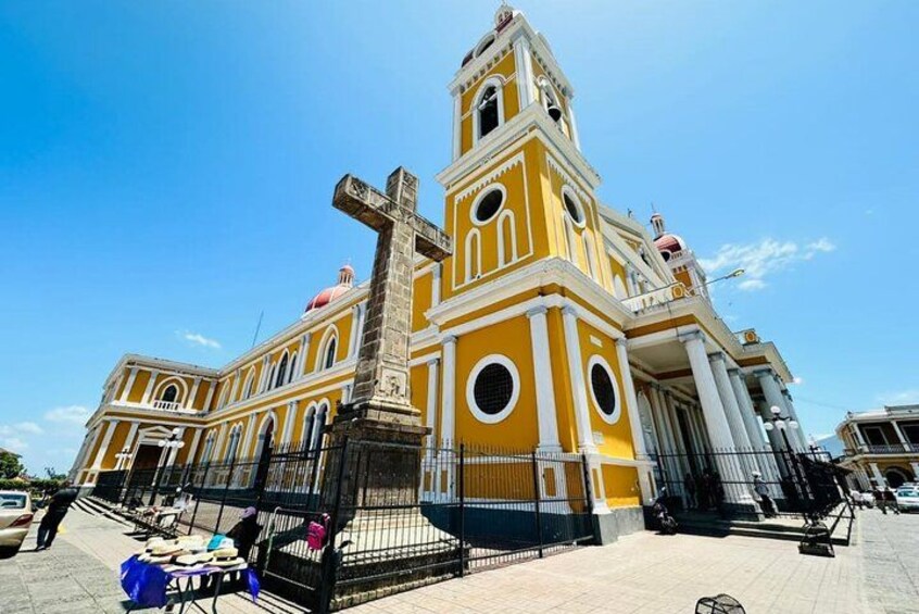 A yellow church with a bell tower and a large cross in front. 1