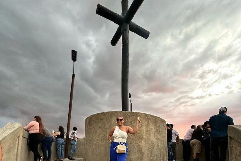 A large cross structure, a cloudy sky, and people standing around. 3