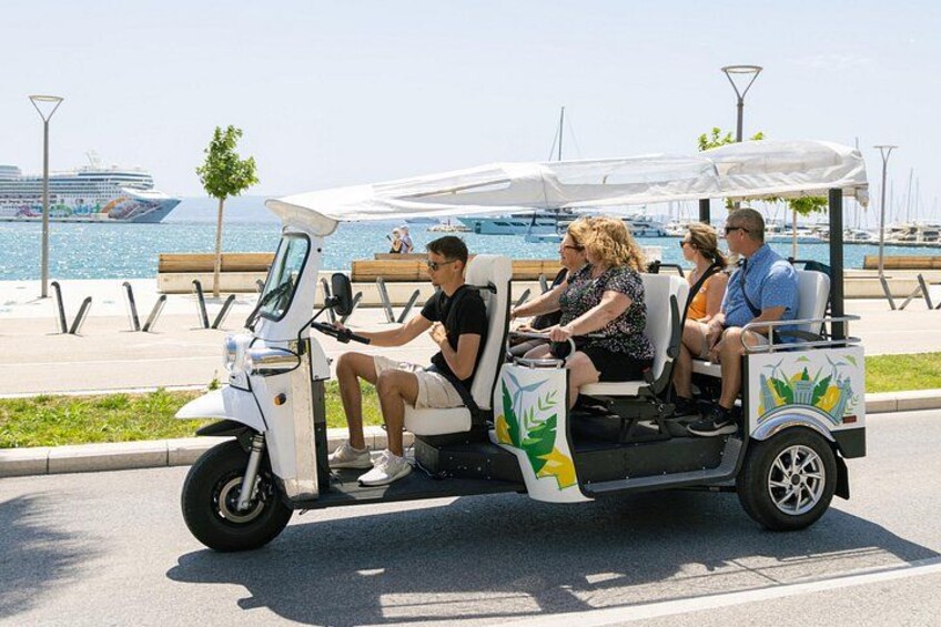 Een golfkarretje met passagiers op een zonnige dag, bij een jachthaven met boten op de achtergrond. 3