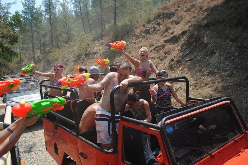Personas en un vehículo con pistolas de agua, una ladera boscosa y terreno rocoso. 2