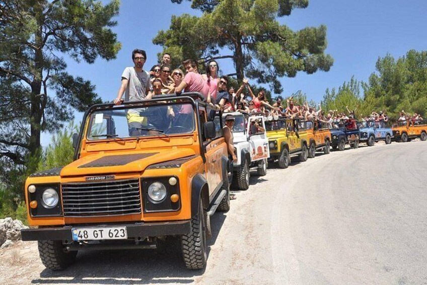 Una caravana de vehículos Land Rover con pasajeros circulando por un camino bordeado de árboles. 3