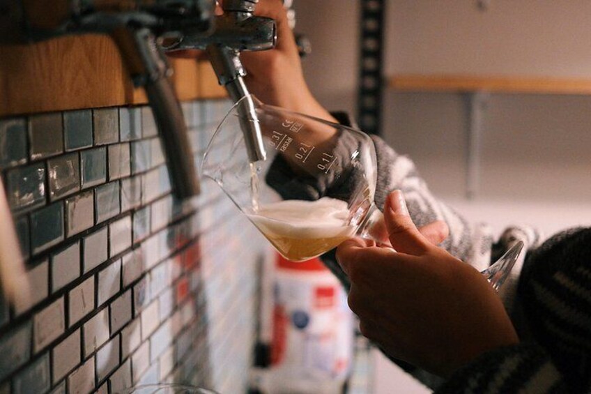 Iemand giet een drankje uit een kraan in een maatglas. 1