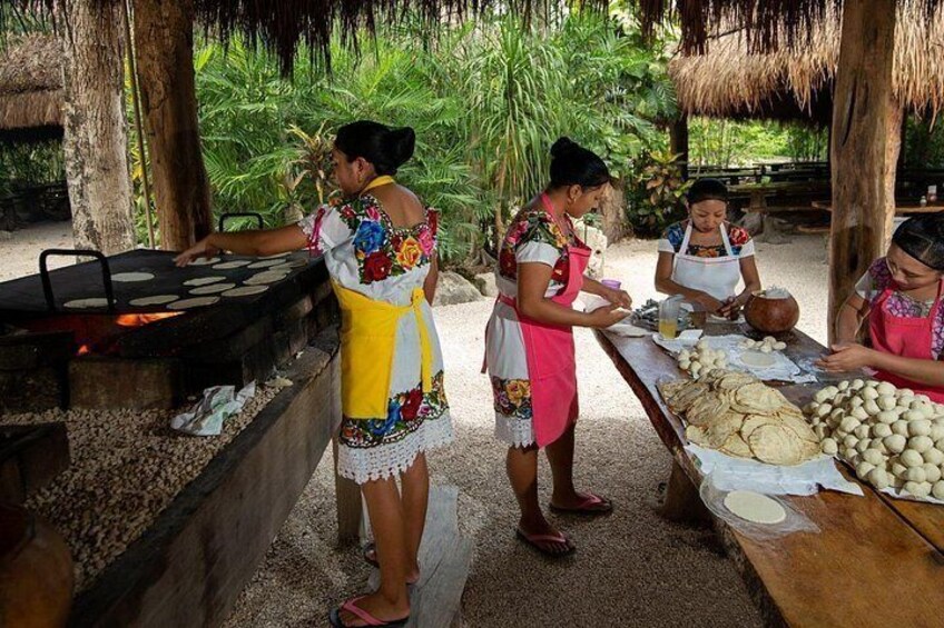 Women preparing food outdoors, with a grill and tortillas on a table. 5