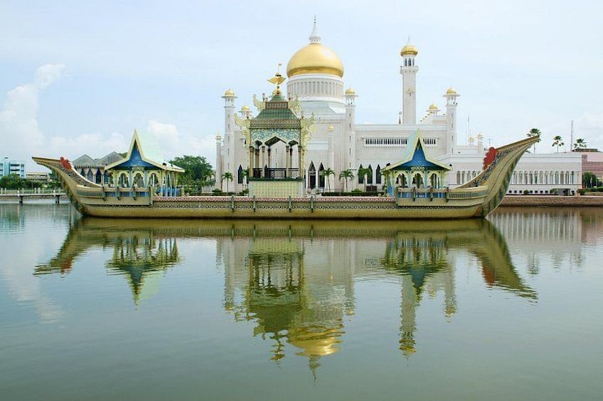 A mosque with a golden dome and minarets, a boat with a pointed bow, and reflections in calm water. 3