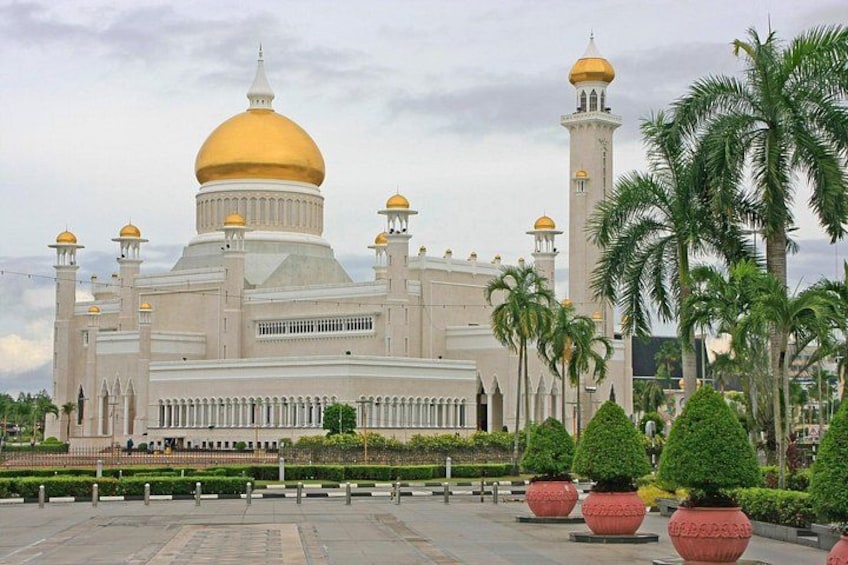 A large mosque with a golden dome and minarets, surrounded by palm trees and potted plants. 1