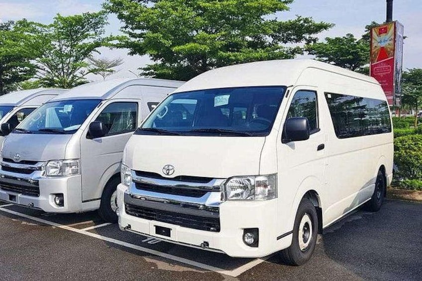 A row of white Toyota vans parked in a lot with trees and a billboard in the background. 4