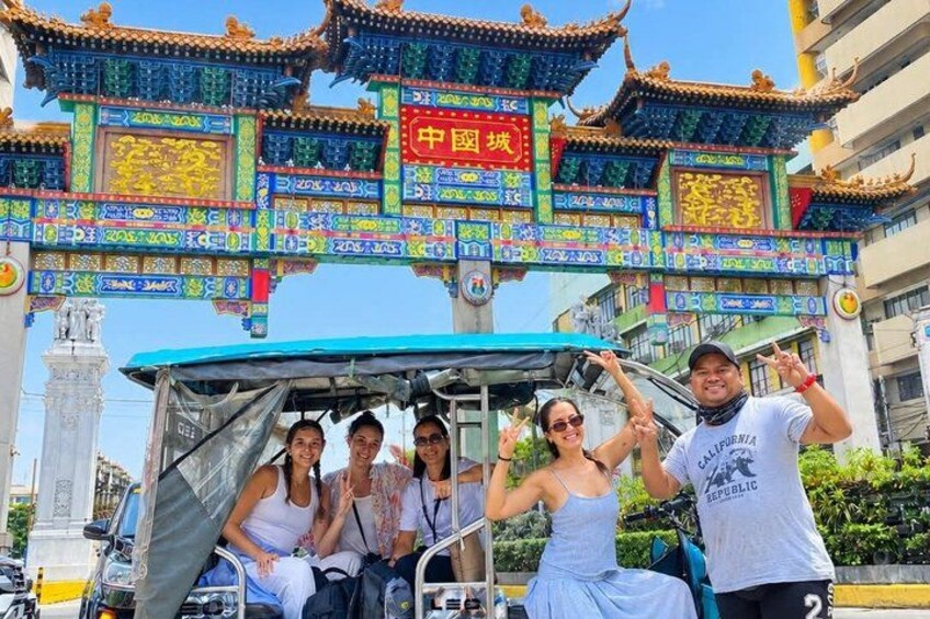 Een groep mensen in een voertuig, met een traditionele Chinese poort op de achtergrond. 1