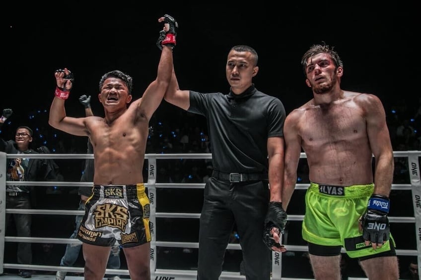 A boxing match with a referee and two boxers in a ring. 2