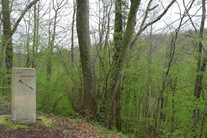 Ein steinernes Denkmal mit einem nach rechts zeigenden Pfeil, umgeben von Bäumen und Grün. 3