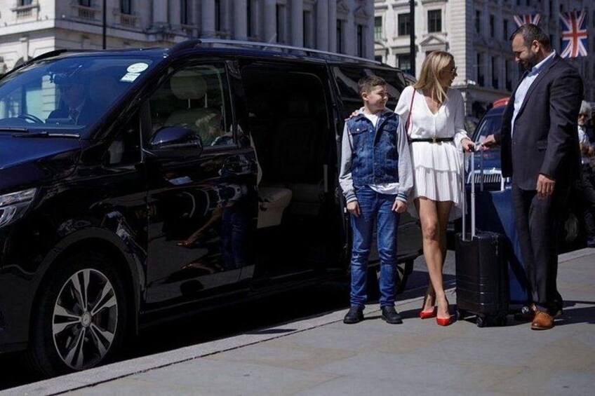A black van parked on a city street with a man and a woman standing next to it, a child in a denim jacket, and a dog on the ground. 2