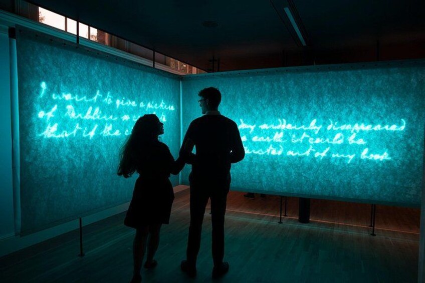 Two people standing in front of a wall with illuminated text. 4