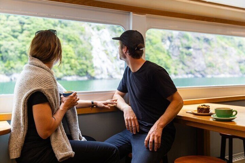 Two people sitting by a window overlooking a body of water and greenery. 2