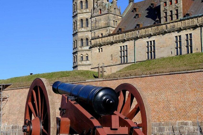 A historical cannon in front of a large, old building with a steep hill behind it. 5