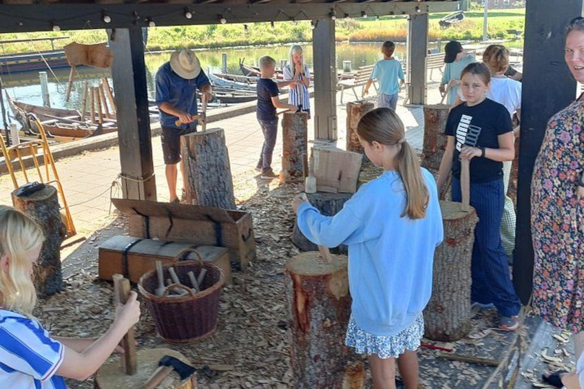 A group of people engaged in wood carving activities outdoors with tools and wood pieces on the ground. 3