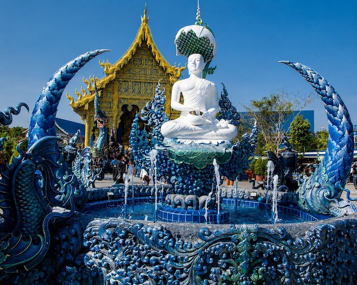 Une grande statue de Bouddha blanche, entourée d’éléments décoratifs bleus et verts, avec un bâtiment traditionnel thaïlandais en arrière-plan. 3