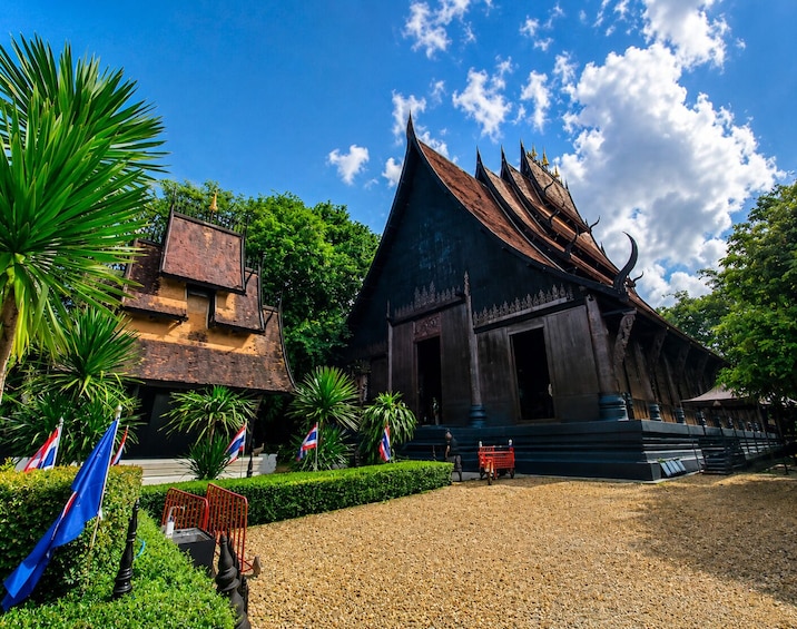 Un temple thaïlandais traditionnel, doté d’un toit à forte pente, entouré d’une végétation luxuriante et de mâts de drapeaux. 2