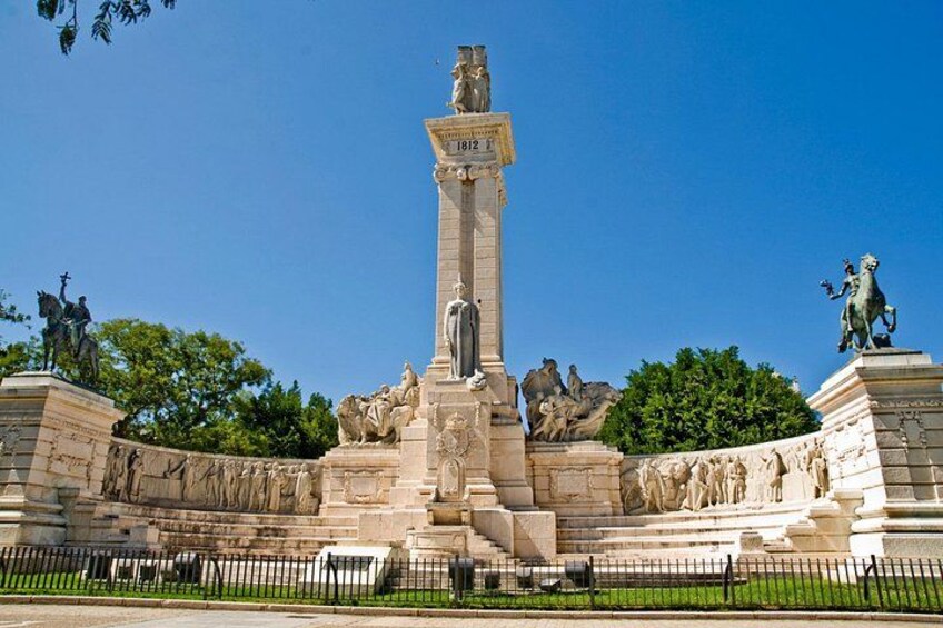 Un grand monument orné, avec une statue centrale, entouré de statues et de reliefs plus petits, situé dans un espace aménagé avec un ciel dégagé. 2