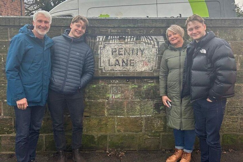 Four people standing in front of a wall with a sign that reads 'Penny Lane.' 2