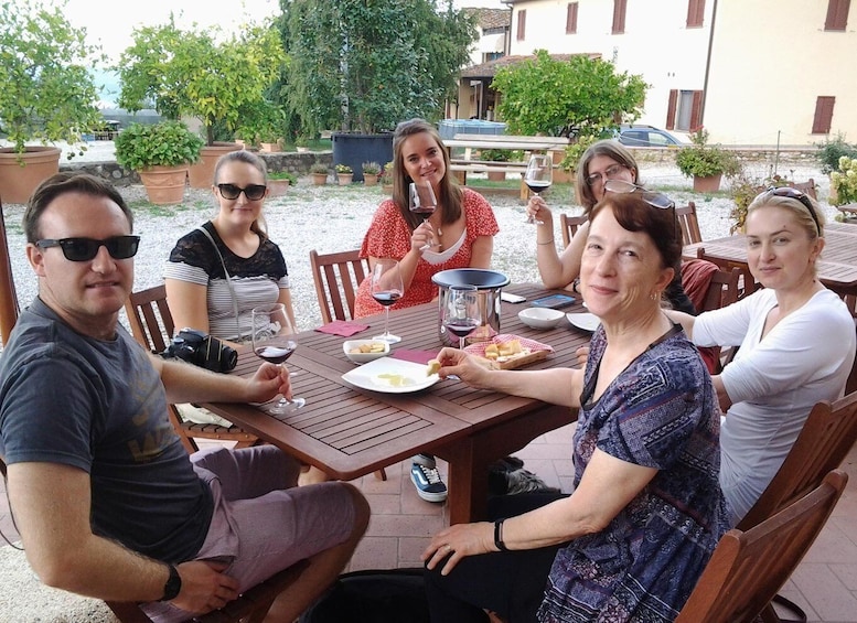 A group of people seated around a wooden table outdoors, with potted plants and a building in the background. 2