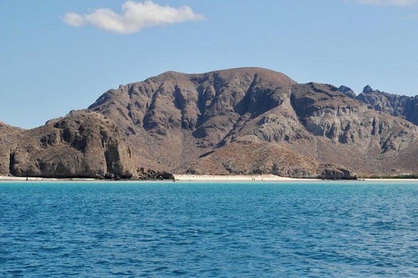 A coastal landscape with a mountain, clear blue water, and a sandy beach. 3