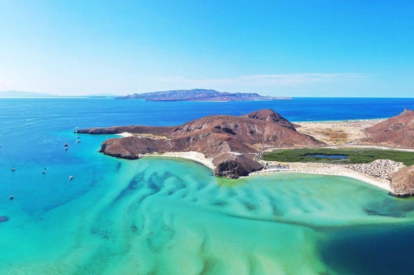 A coastal landscape with clear turquoise waters, rocky outcrops, and distant mountains. 1