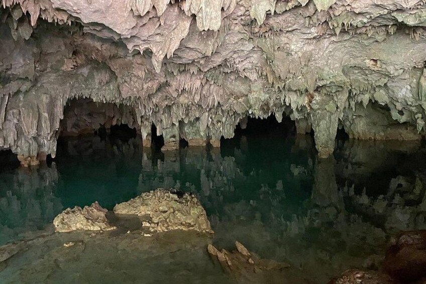 A cave interior with stalactites and stalagmites, a pool of water, and a rocky foreground. 2