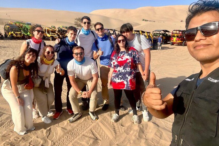 A group of people in a desert with sand dunes and off-road vehicles in the background. 5