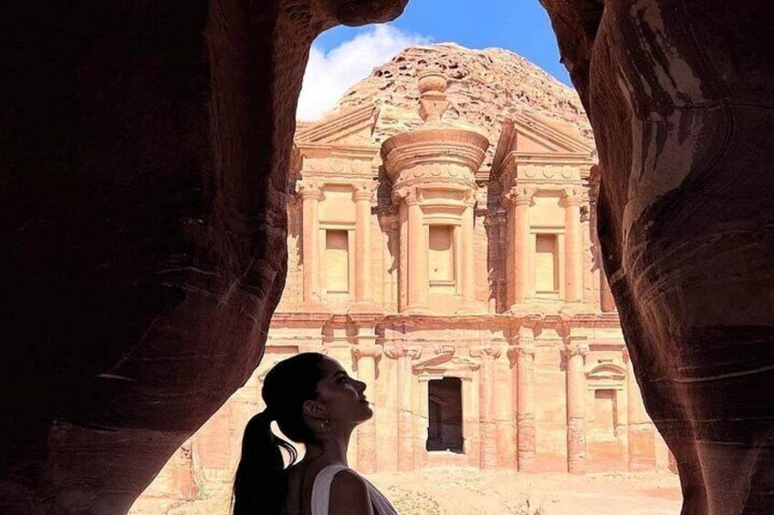 A person standing in a natural rock formation with a historical building in the background. 2