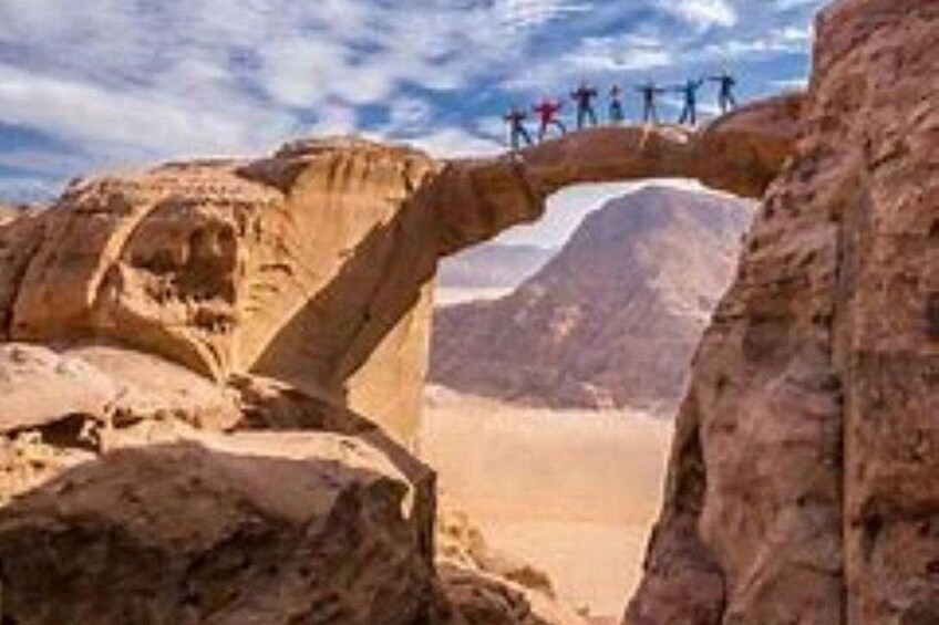 A natural rock arch formation with people standing on top. 4