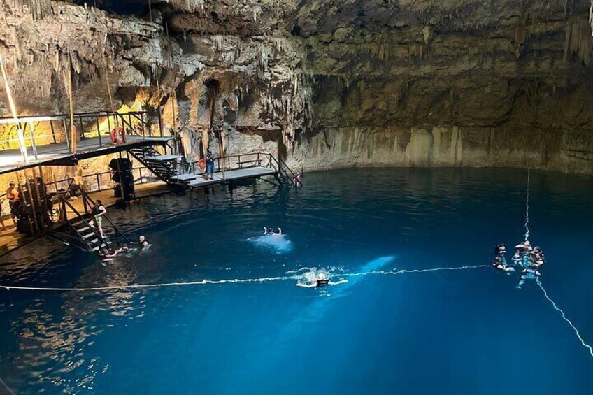 A cave with a swimming pool, a diving platform, and people engaged in water activities. 1