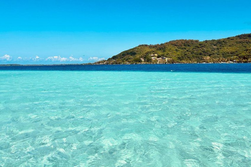 Clear turquoise water, a distant hill with buildings, and a clear blue sky. 1