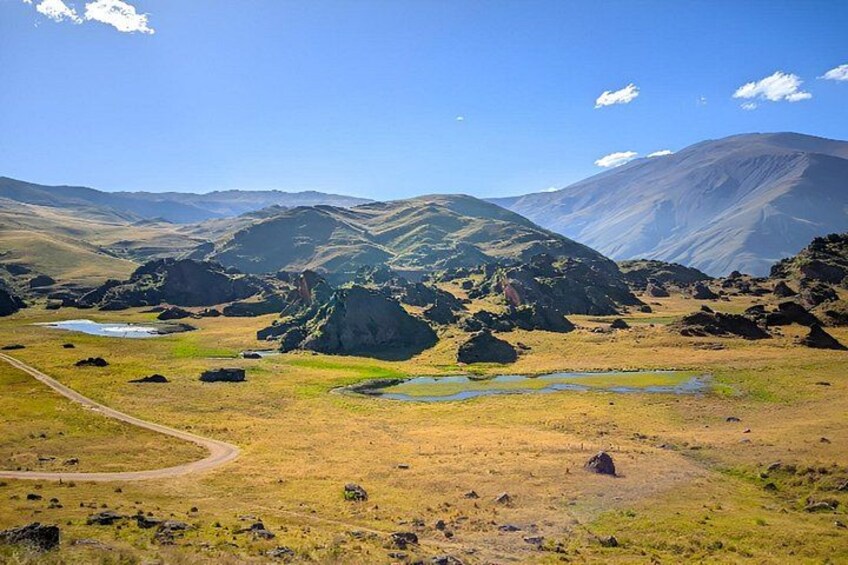 A mountainous landscape with a winding road, rocky outcrops, and small ponds. 4