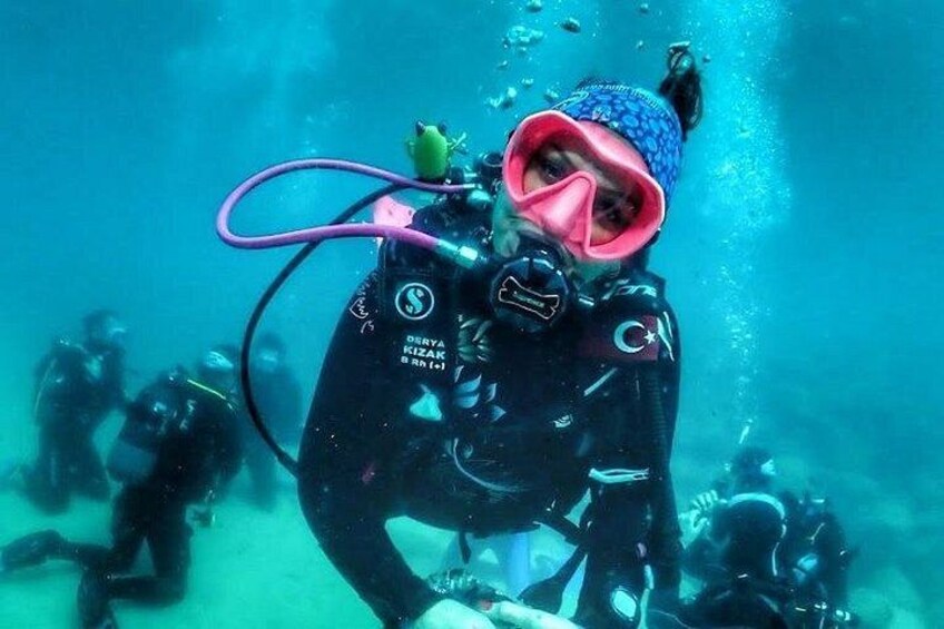 En person dykker med en lyserød snorkel og en blå kasket, omgivet af andre dykkere. 1