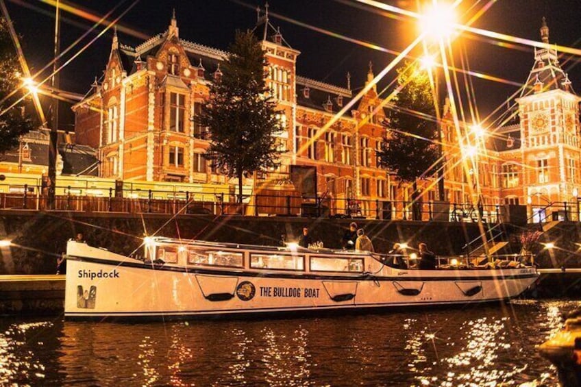 A boat named 'Shipdock' with 'The Bulling Bay' written on it, docked at a waterfront with illuminated buildings in the background. 1