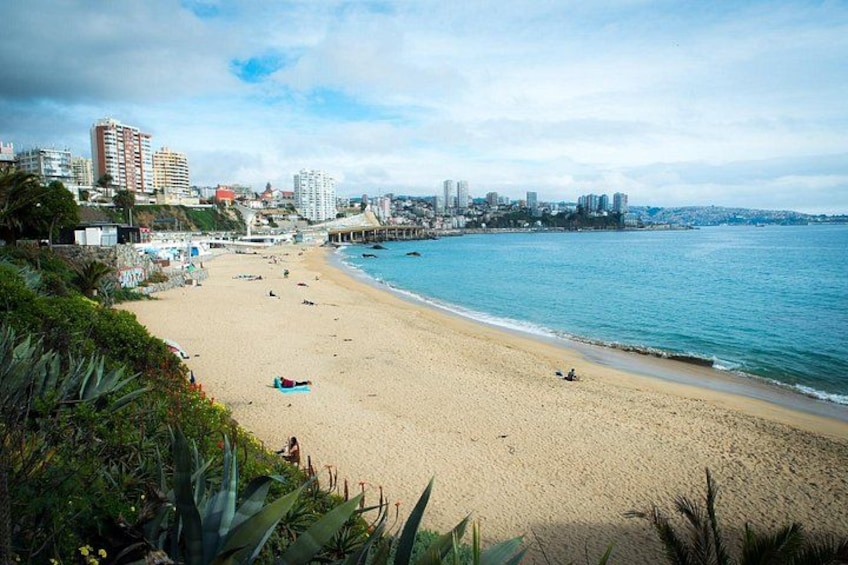 A beach with people, a pier, and buildings in the background. 4