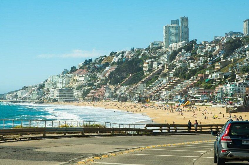 A coastal cityscape with a beach, a road, and a parked car. 1
